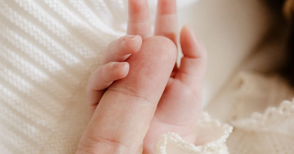 Mão de um bebê recém-nascido segurando o dedo de um adulto sobre um cobertor claro